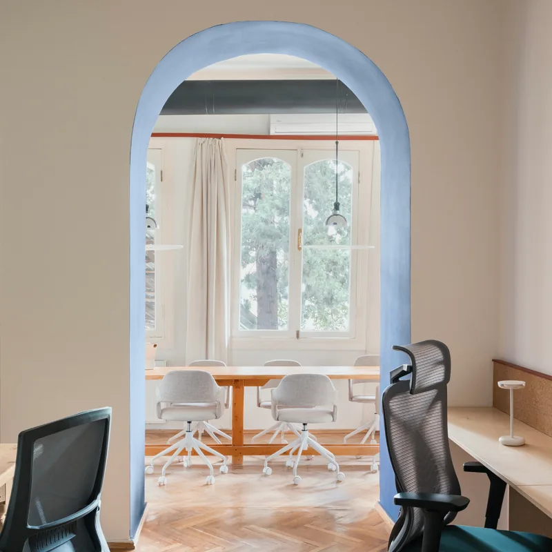Desks and office chairs at Tsre, with a blue archway framing a shared table and tall windows